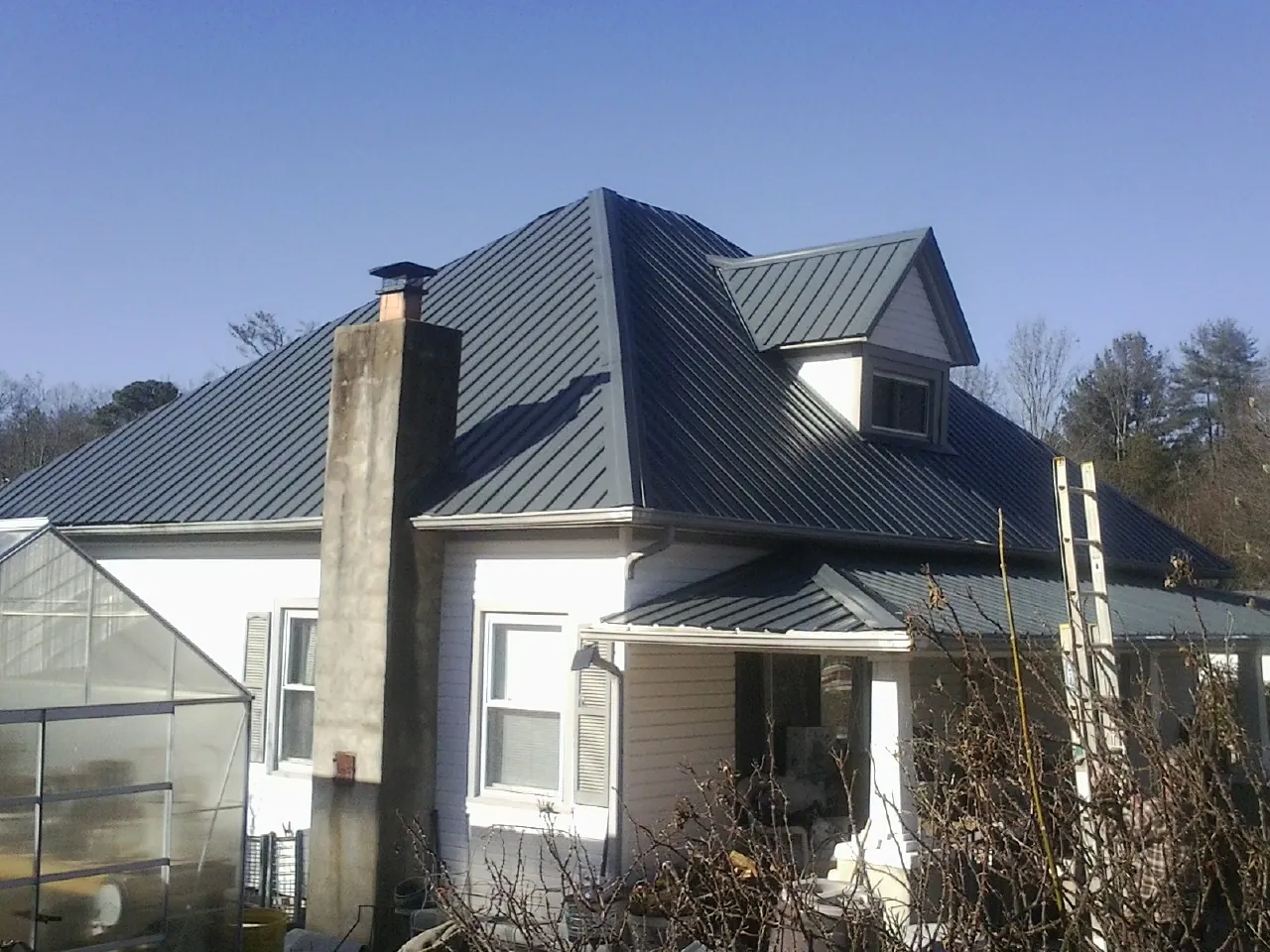 Dark blue standing seam metal roof on a white farmhouse with dormer — Slate & Tile Roof Repair by Roofing Brothers in Coalport