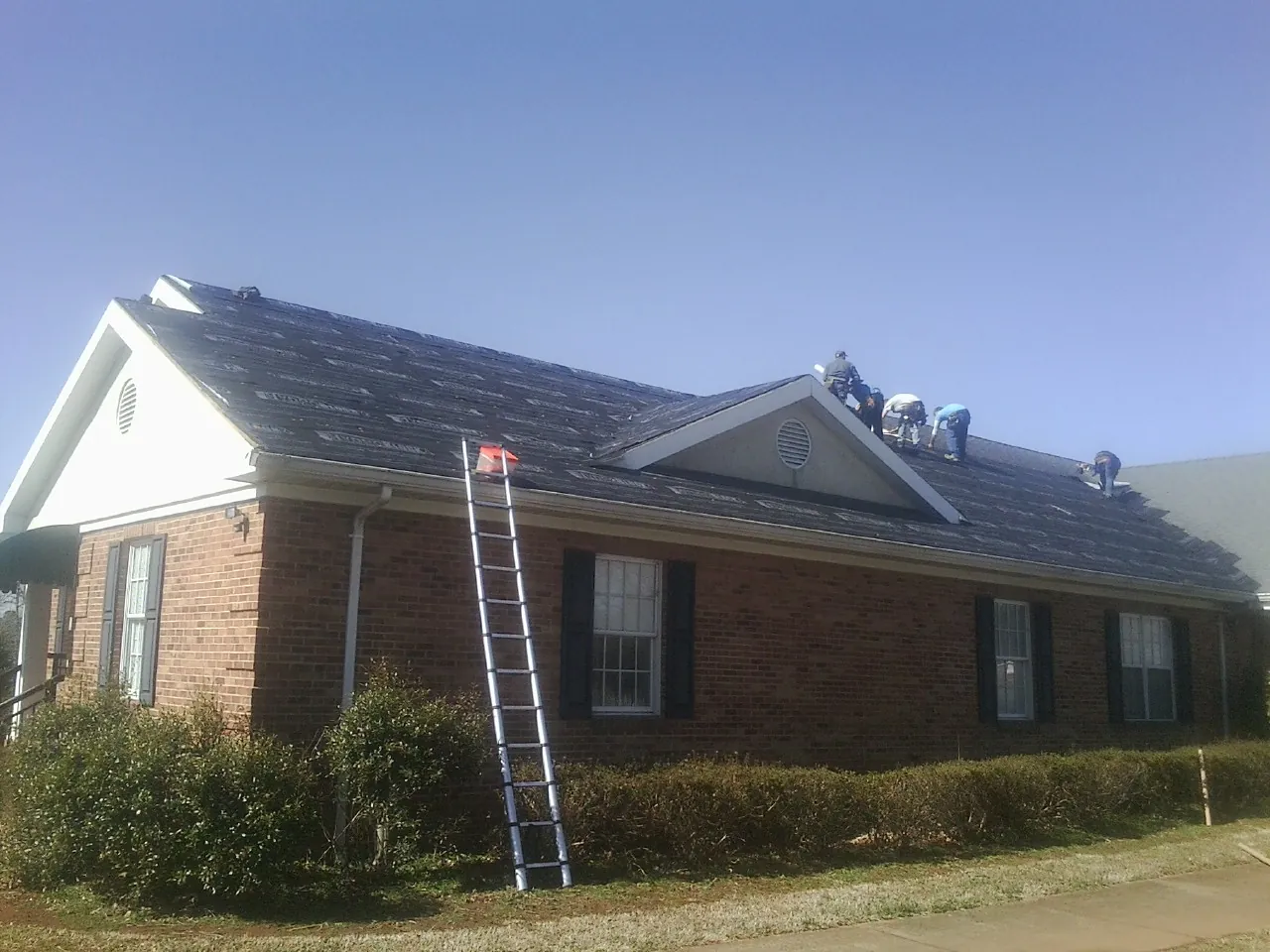 Crew tearing shingles off a brick ranch roof with a ladder set — Emergency Roof Repair work by our crew in Coalport