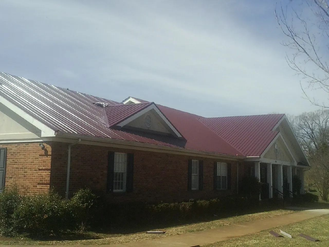 Red metal roof with gabled entries on a long brick building, from a Hail Damage Roof Repair job in Coalport