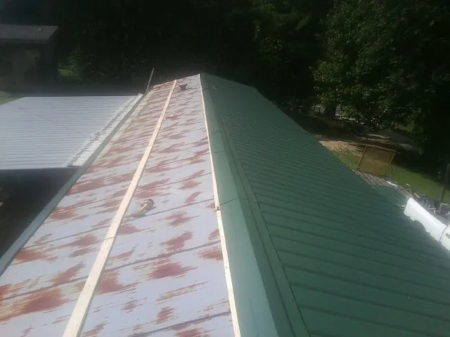 Old rusted panels beside newly installed green metal roofing — Wind Damage Roof Repair by Roofing Brothers in Coalport