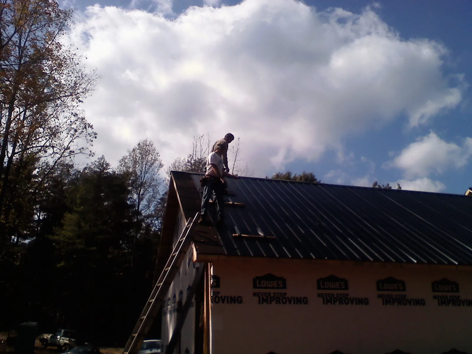 Roofer fastening dark metal panels high against a cloudy sky in Coalport