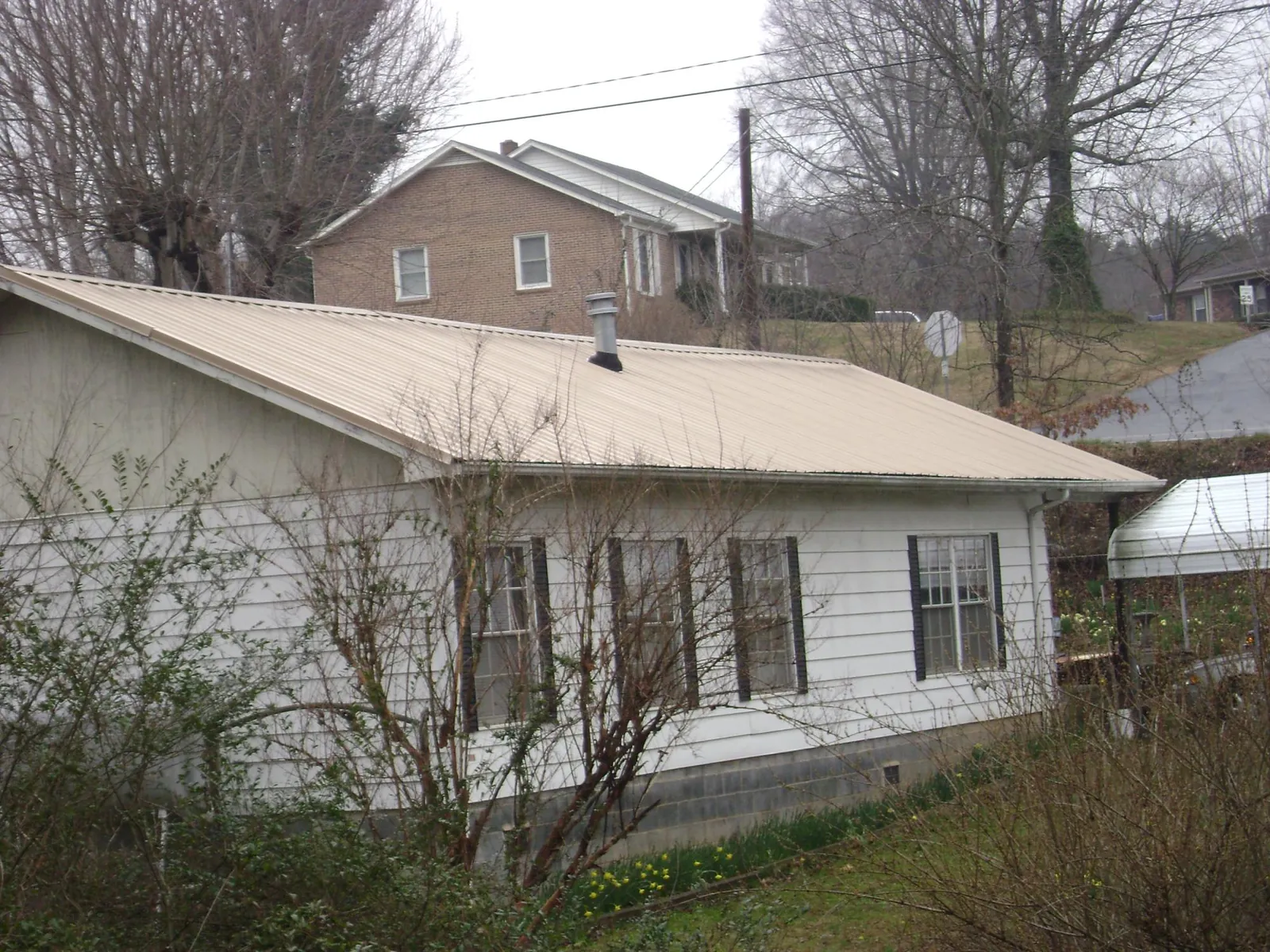 Tan metal roof on a white sided house set into a hillside — Commercial Roofing by Roofing Brothers in Coalport